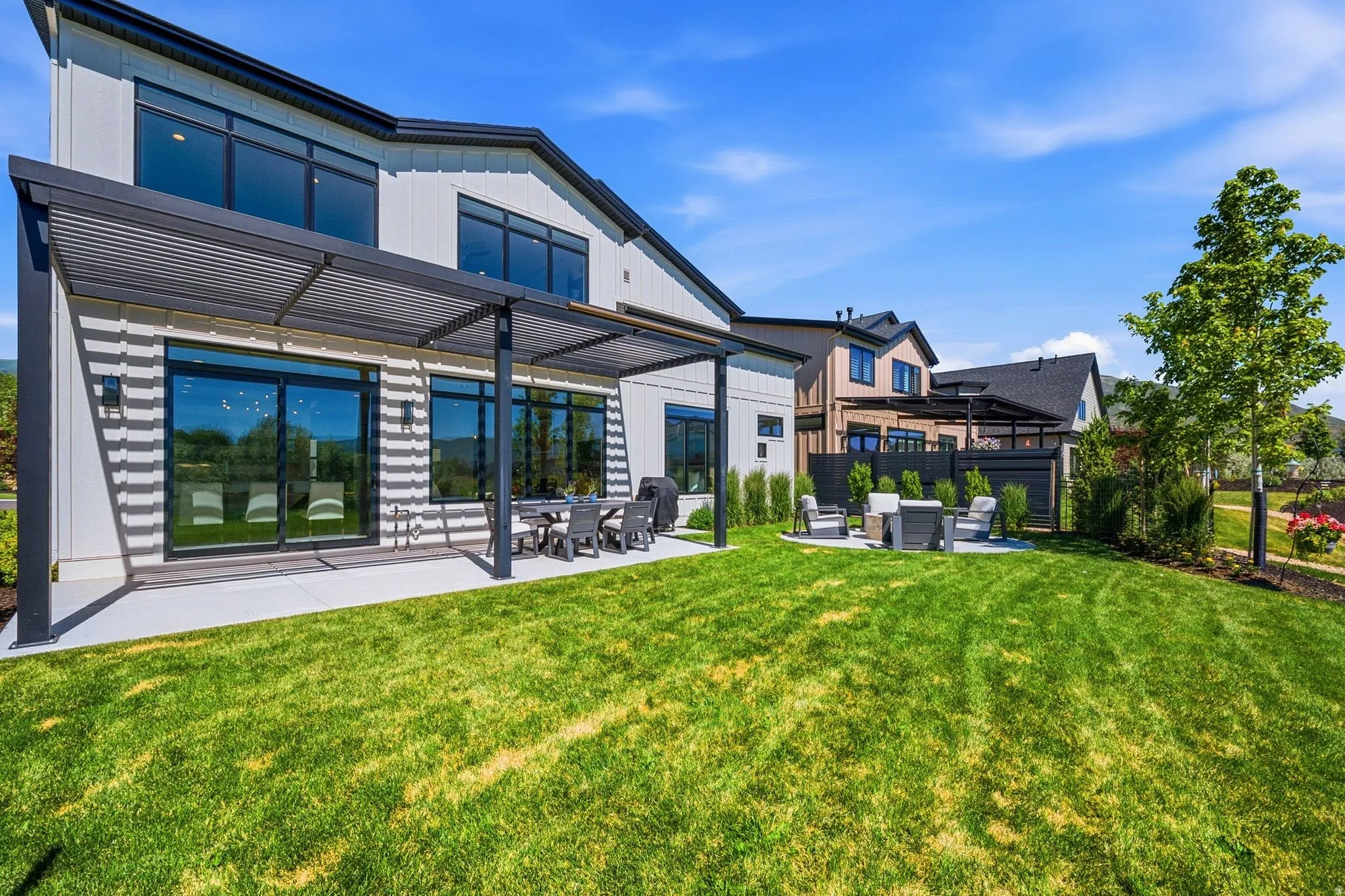 Expansive green lawn with a concrete patio featuring an attached louvered pergola