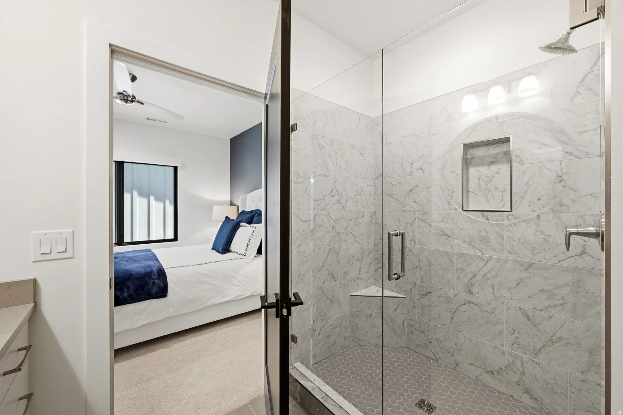 Glass-enclosed shower with large format tile surround, hexagon tile flooring, and integrated shower niche