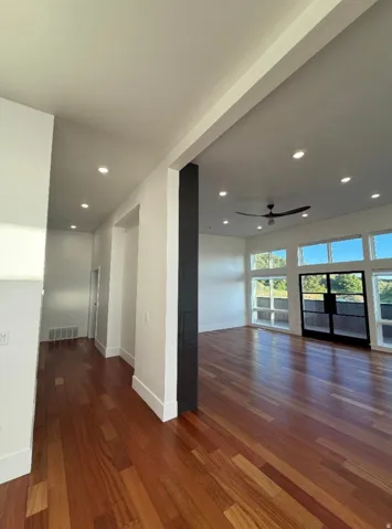 Expansive open-concept living space featuring rich wood flooring, abundant natural light from numerous windows, recessed lighting, and a modern ceiling fan