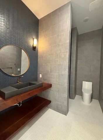 Powder room featuring a herringbone pattern accent wall, a floating wood vanity with an integrated basin sink, a wall-mounted light fixture, and white penny tile flooring