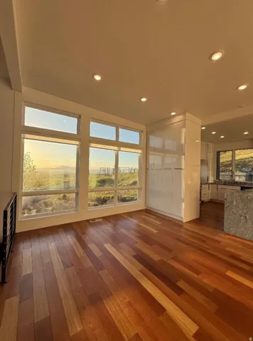 Spacious interior featuring wood-finish flooring, a wall of large windows, recessed lighting, white built-in cabinetry, and a stone-clad island