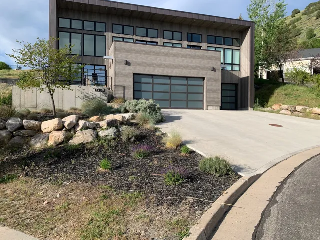 Modern architectural exterior featuring multiple large windows, a two-car garage with frosted glass panels, an additional single-car garage with a frosted glass panel, and a concrete driveway