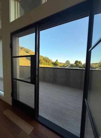 Expansive sliding glass doors open to an outdoor terrace featuring a textured floor and a low-profile perimeter wall