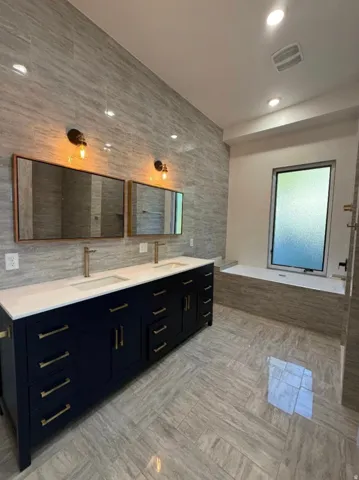 Spacious bathroom featuring a double vanity with dark cabinetry and gold-tone hardware, a white countertop with dual sinks, and gold-tone faucets