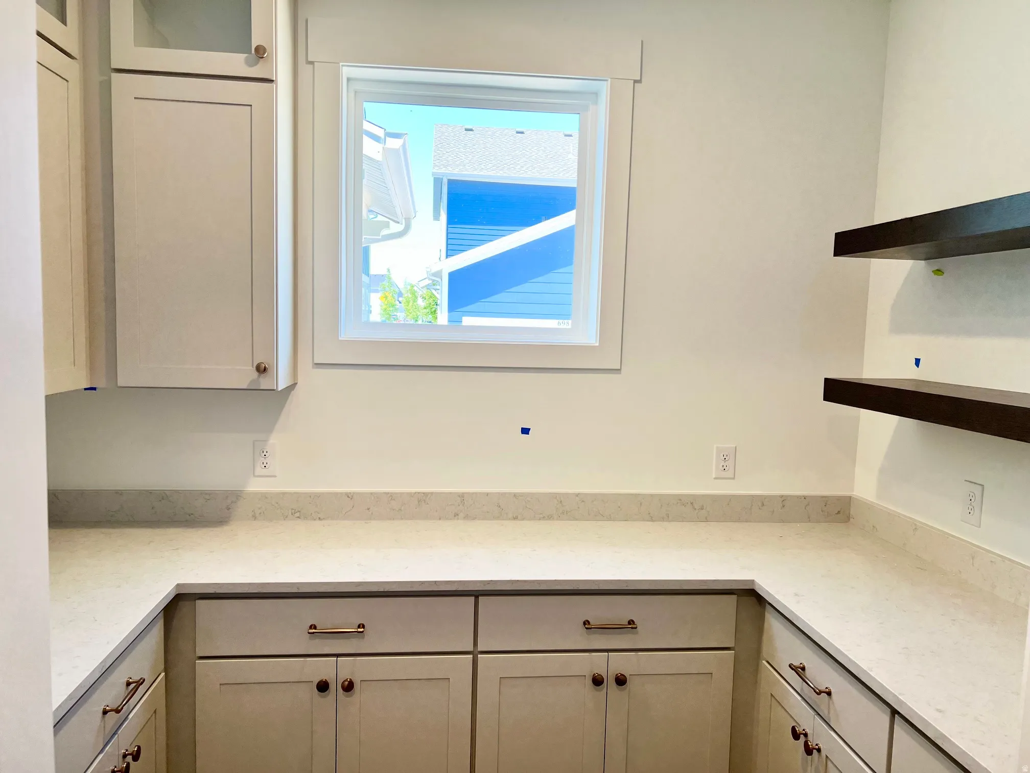 L-shaped countertop with light-toned surface, light-colored cabinetry with varied hardware, and dark floating shelves