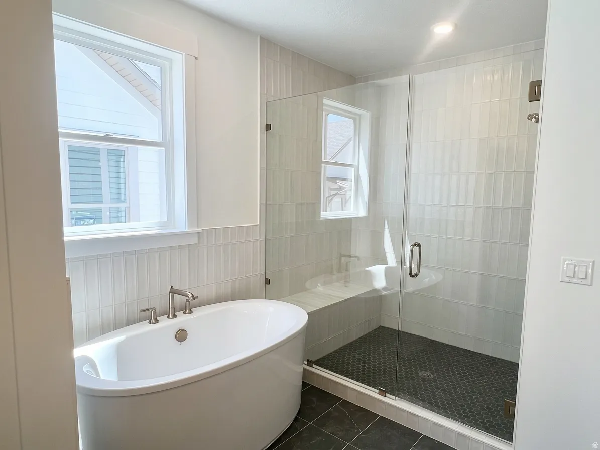 Freestanding oval soaking tub with brushed nickel fixtures, glass-enclosed shower with a built-in bench, and black hexagonal mosaic tile flooring