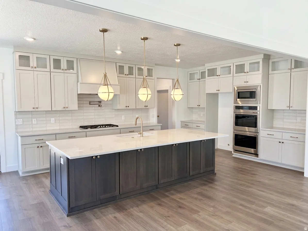 Spacious kitchen featuring an expansive central island with a light-toned countertop, contrasting dark wood-finish cabinetry, and three spherical pendant lights