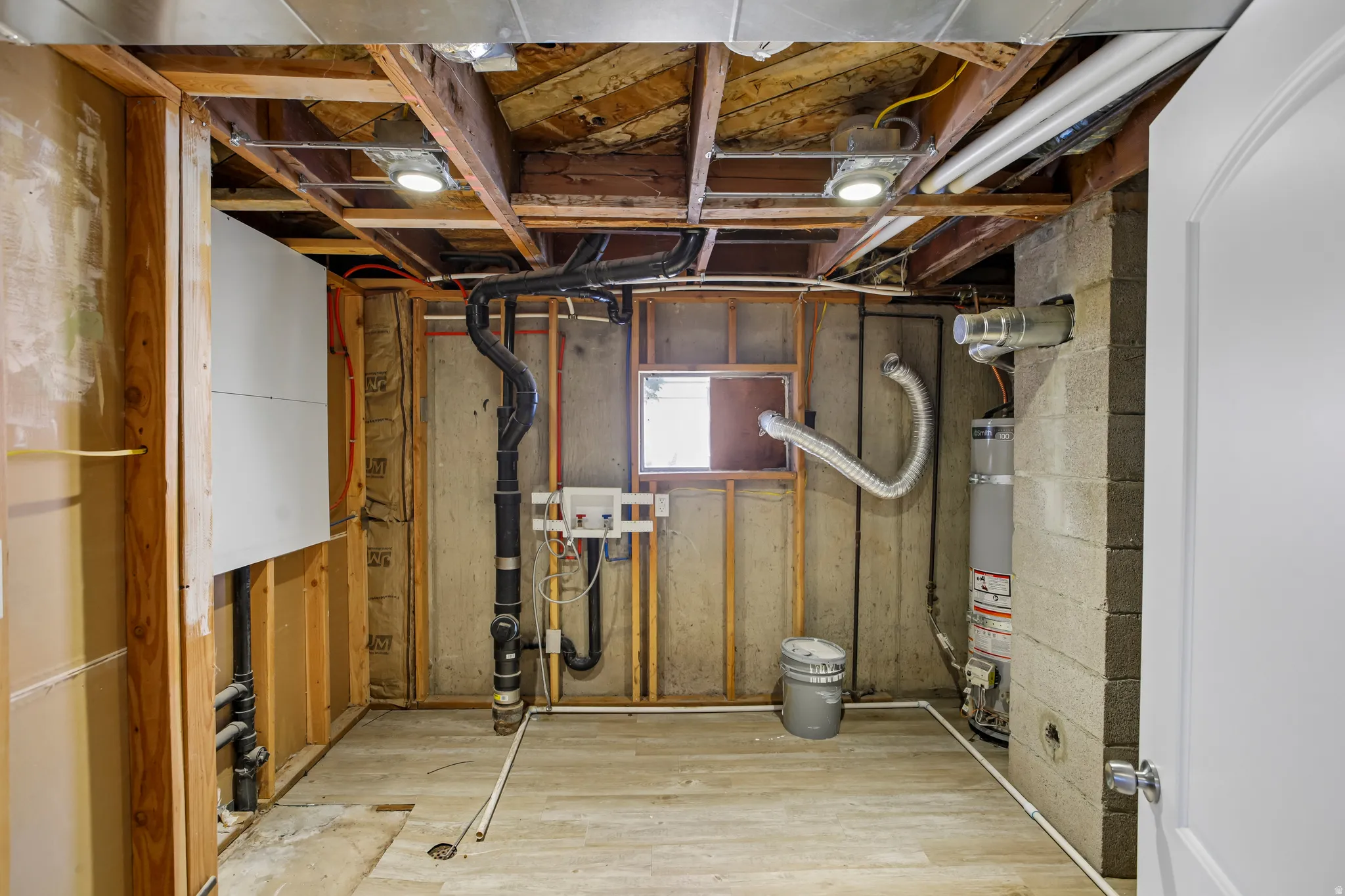 Unfinished basement space featuring exposed wood framing, concrete block foundation walls, and wood-finish flooring