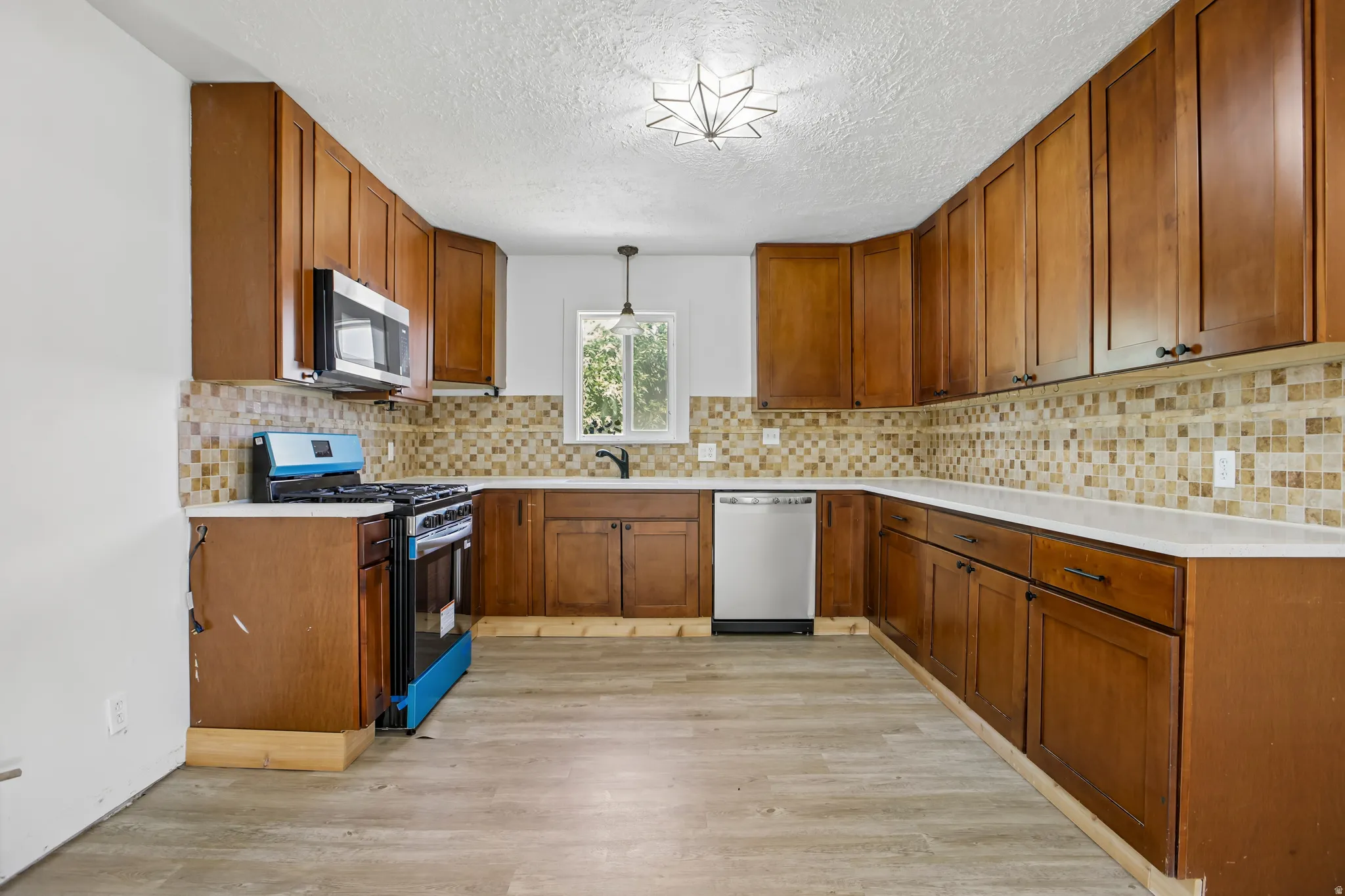 Kitchen featuring wood cabinetry, light-toned countertops, a mosaic tile backsplash, stainless steel appliances, and wood-finish flooring