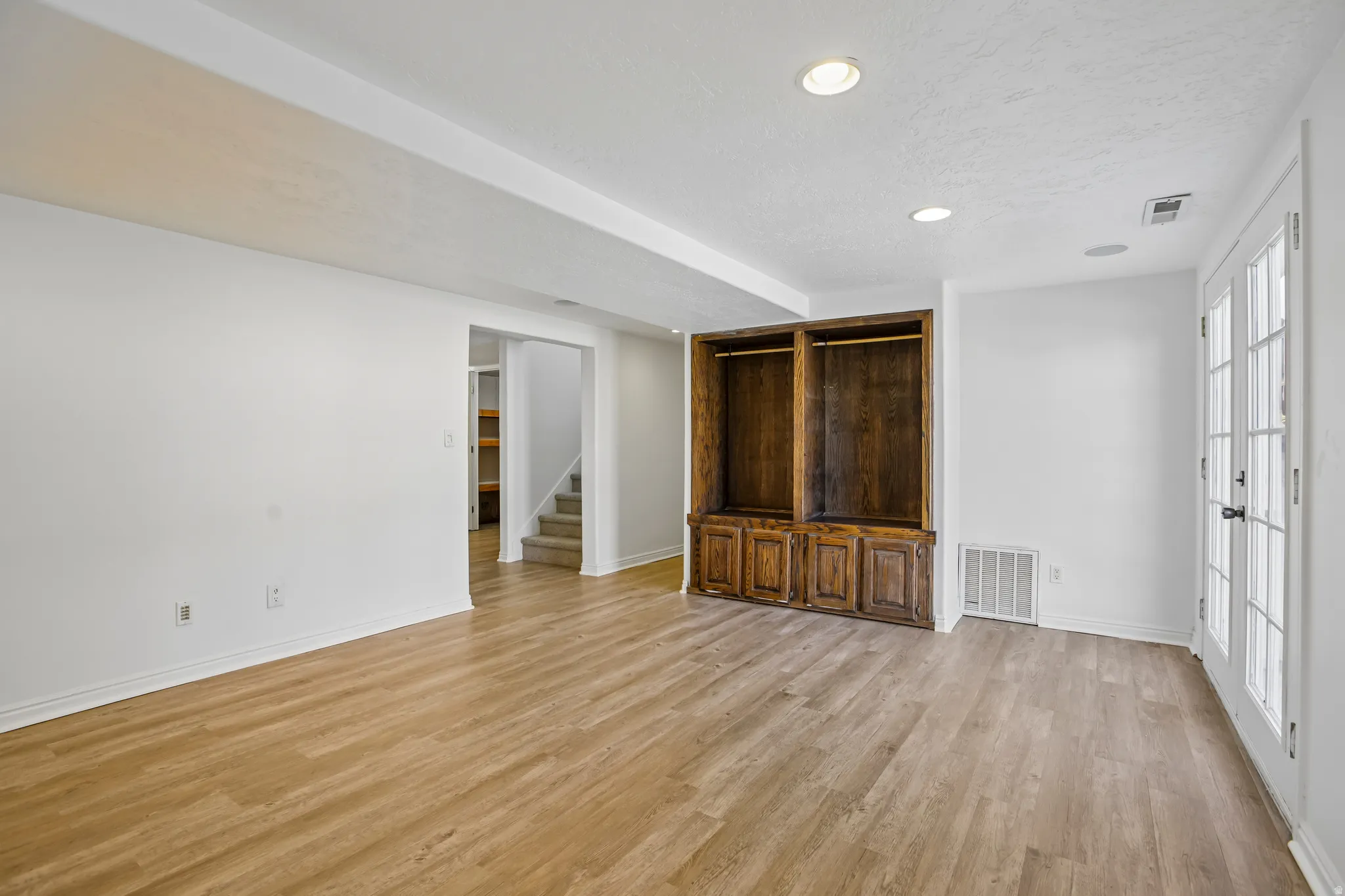 Spacious room featuring wood-finish flooring, recessed lighting, and a built-in wooden cabinet with open shelving and lower storage