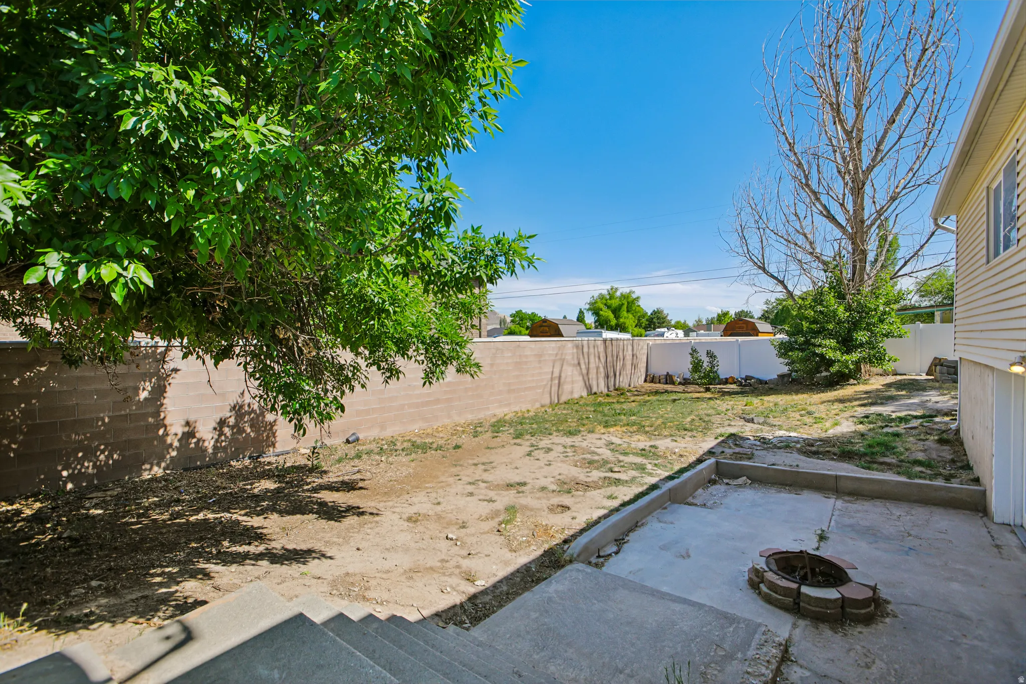 Backyard featuring a concrete patio, built-in fire pit, and mature shade tree