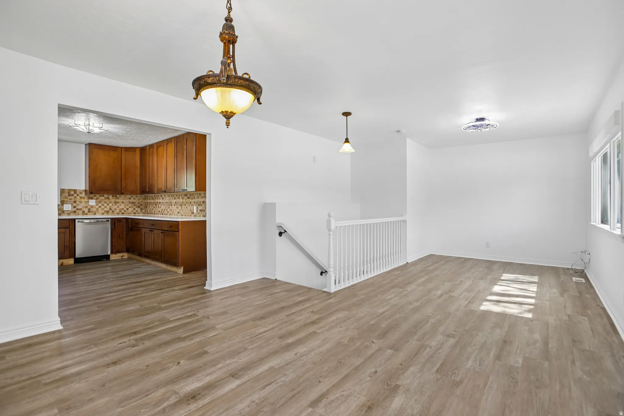Open-concept living area with wood-finish flooring, white painted walls, and a staircase featuring a white railing