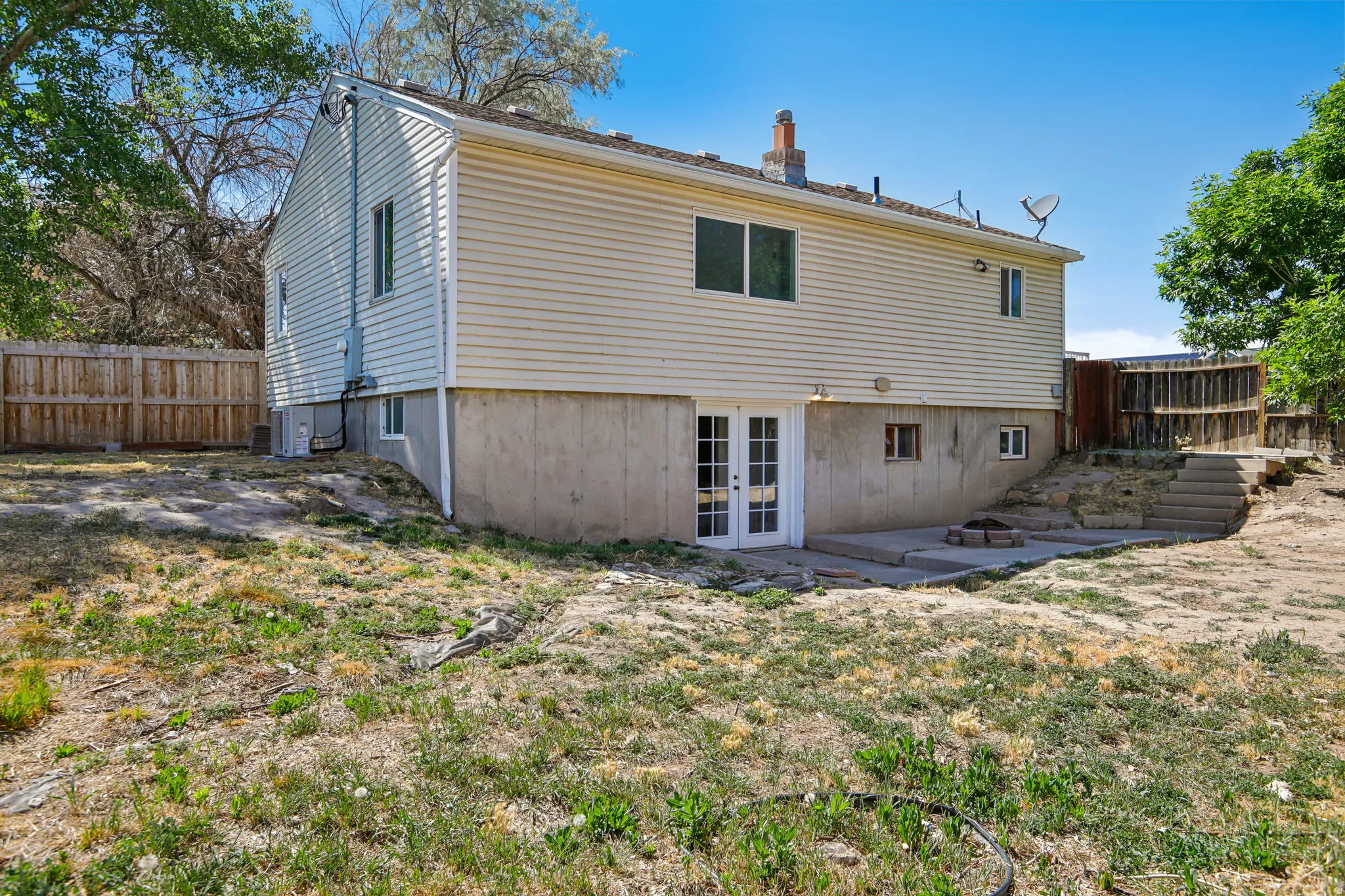 Rear exterior featuring light-colored siding, a concrete patio, and a wood privacy fence
