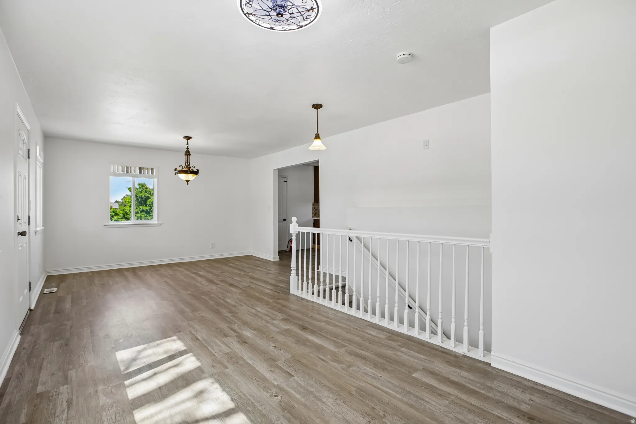 Spacious interior featuring wood-finish flooring, white painted walls, and a white baluster railing