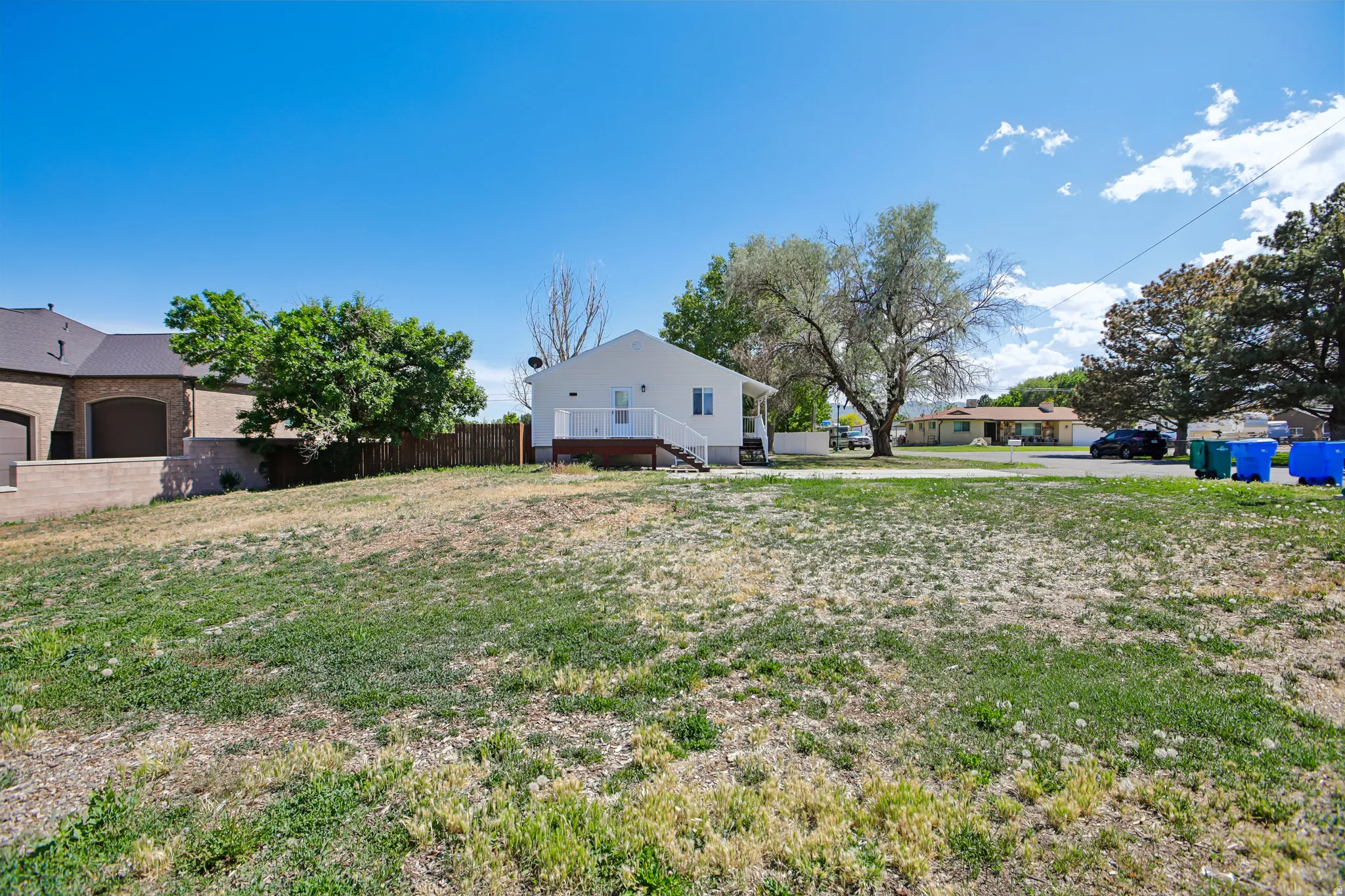 Expansive grassy lot with a white exterior home featuring a rear deck and mature trees