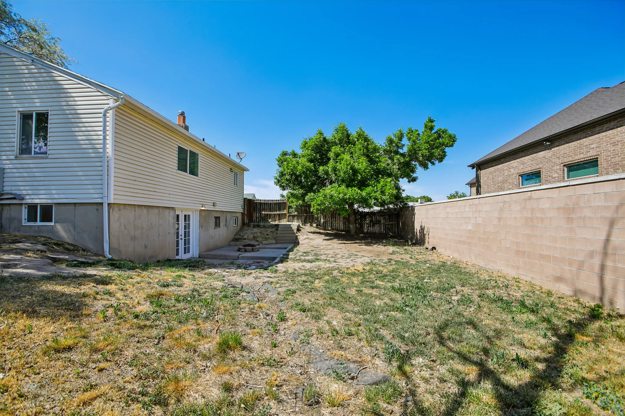 Spacious backyard featuring a concrete block wall, mature tree, multi-level concrete patio, and a double glass door entry