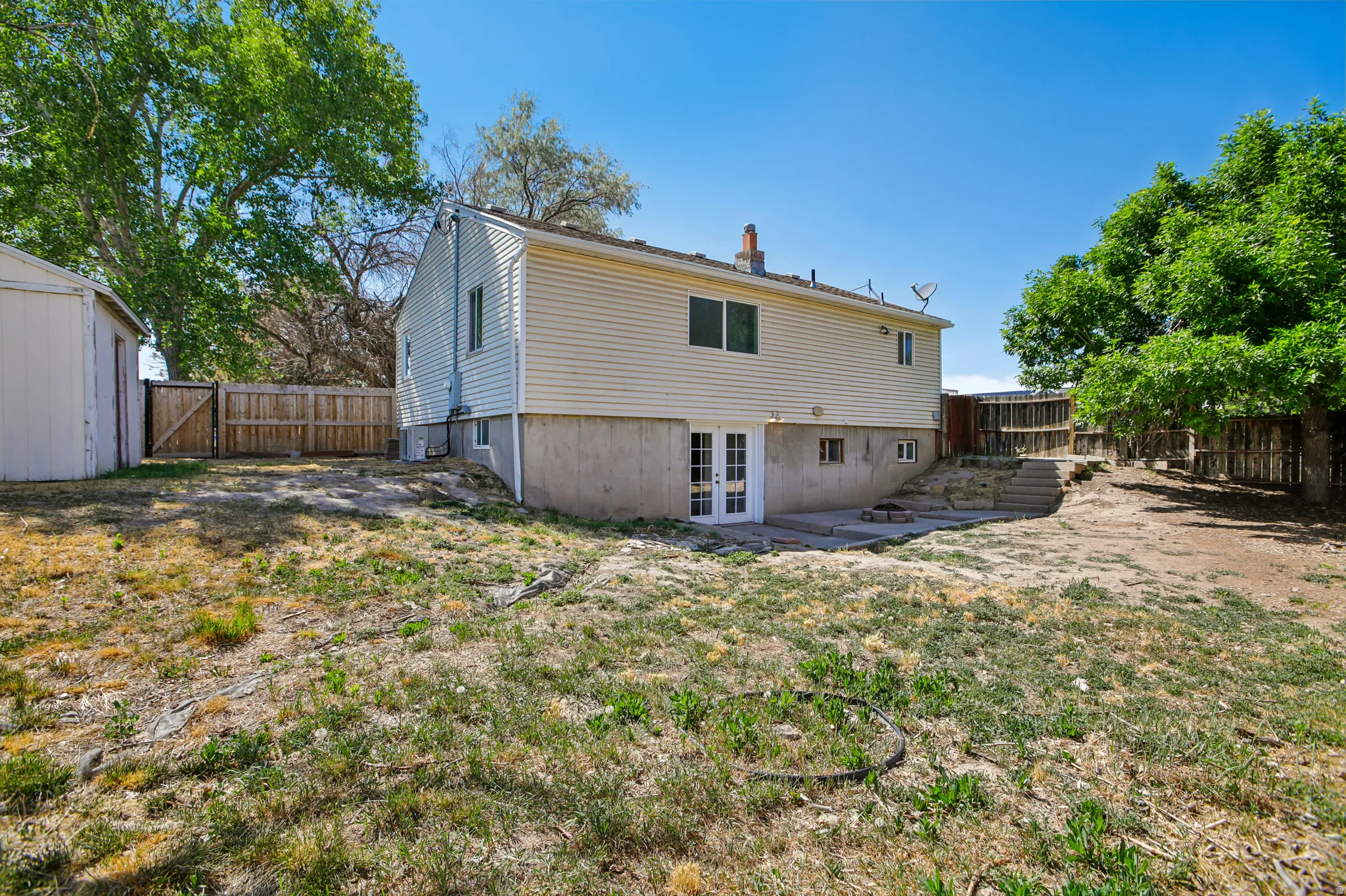 Expansive backyard featuring a wood privacy fence, mature trees, and a concrete patio with exterior access