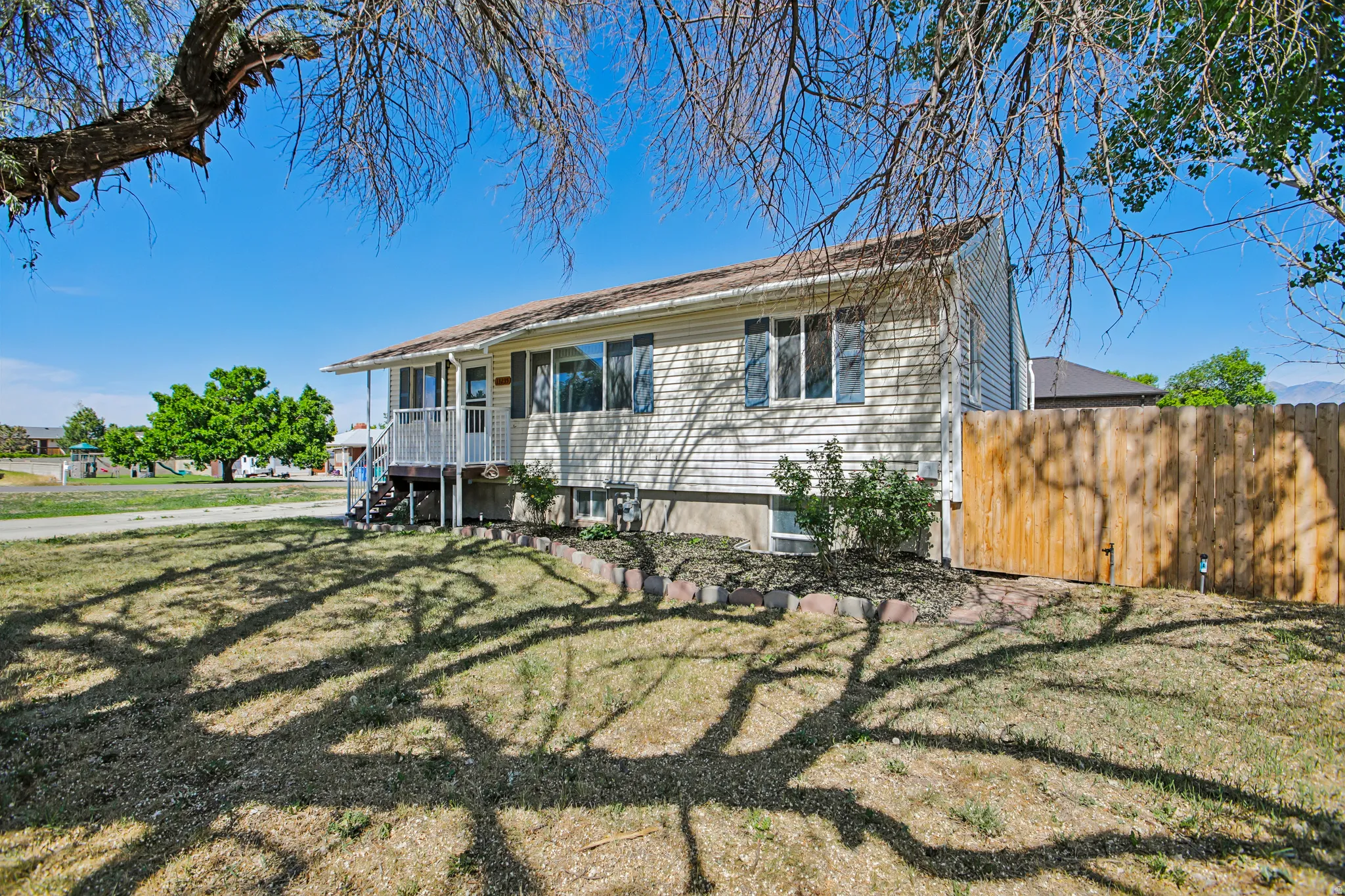 Split-level residence featuring light-toned siding, a covered front porch with white railings, and a natural wood privacy fence