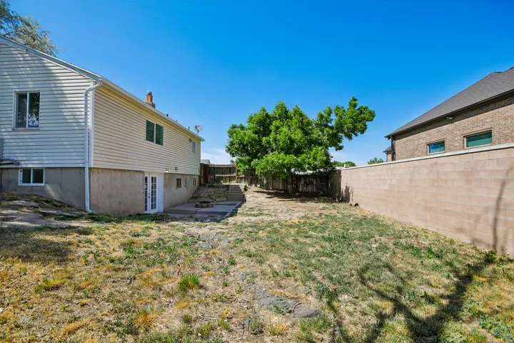 Spacious backyard featuring a concrete block wall, mature tree, multi-level concrete patio, and a double glass door entry