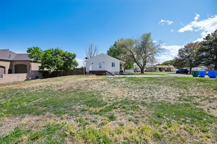 Expansive grassy lot with a white exterior home featuring a rear deck and mature trees