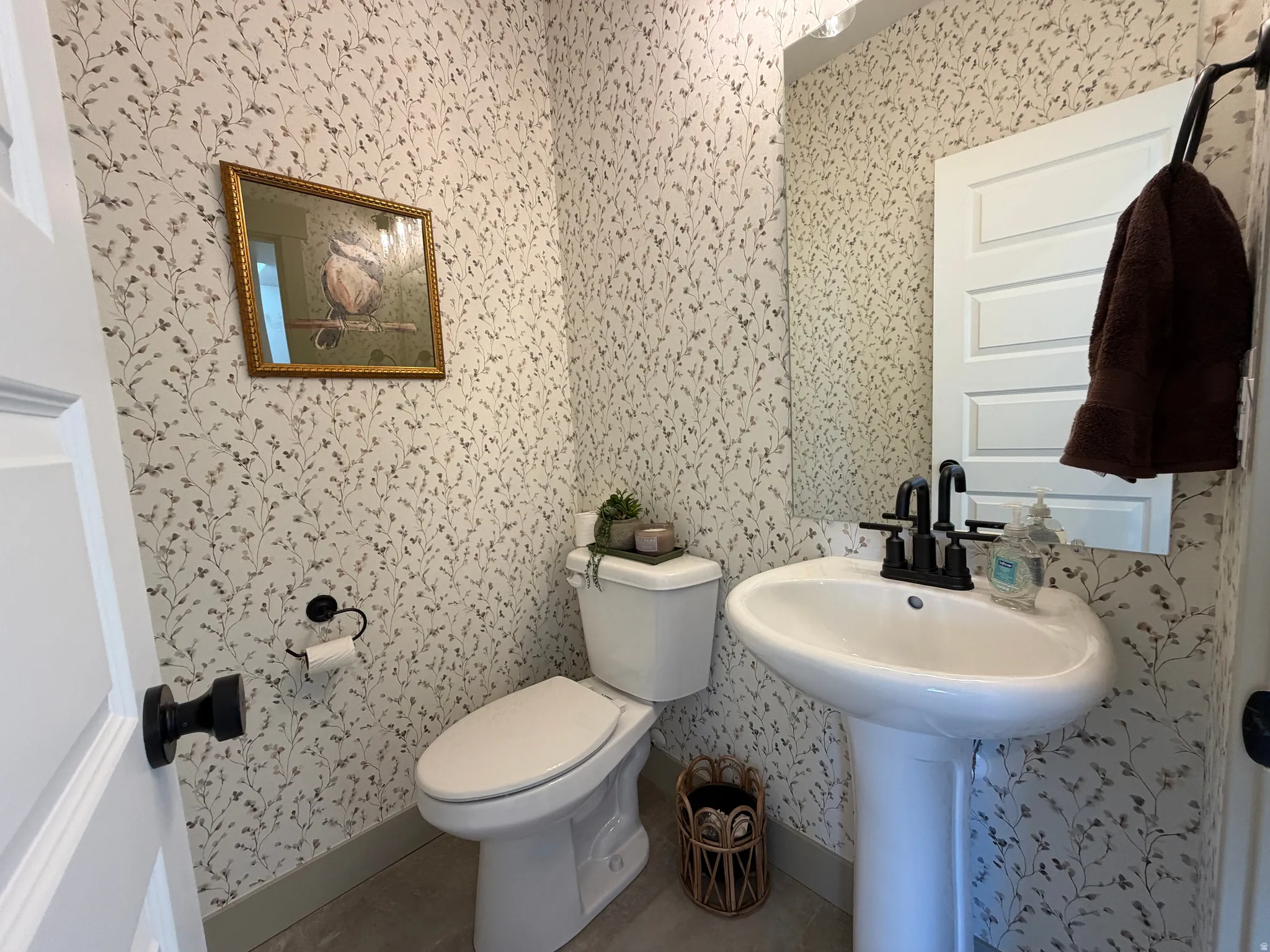Powder room featuring a pedestal sink with matte black faucet, wall-mounted mirror, and botanical print wallpaper