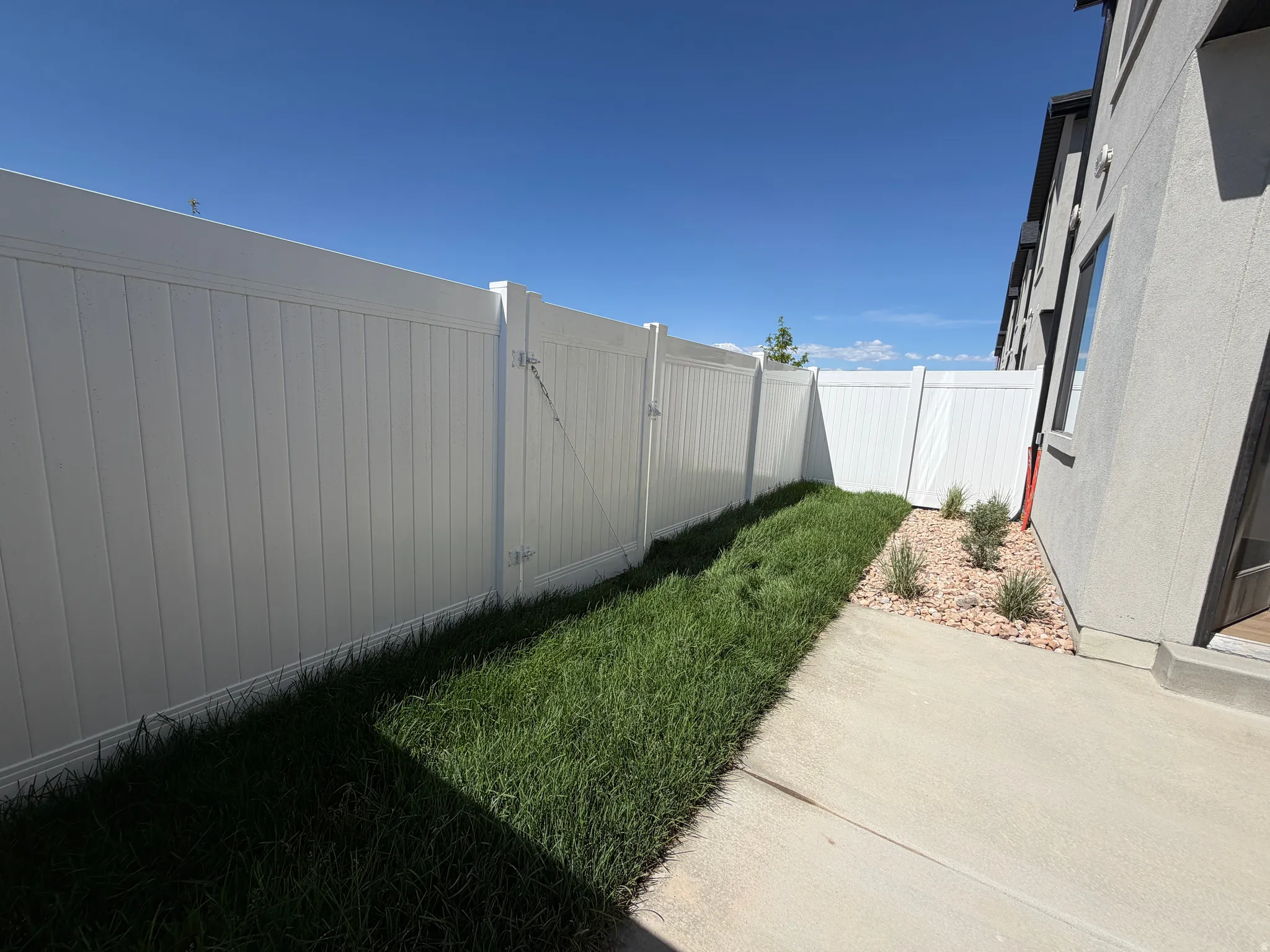 Private outdoor space featuring a full-height white fence, concrete patio, and landscaped area with grass and decorative rocks