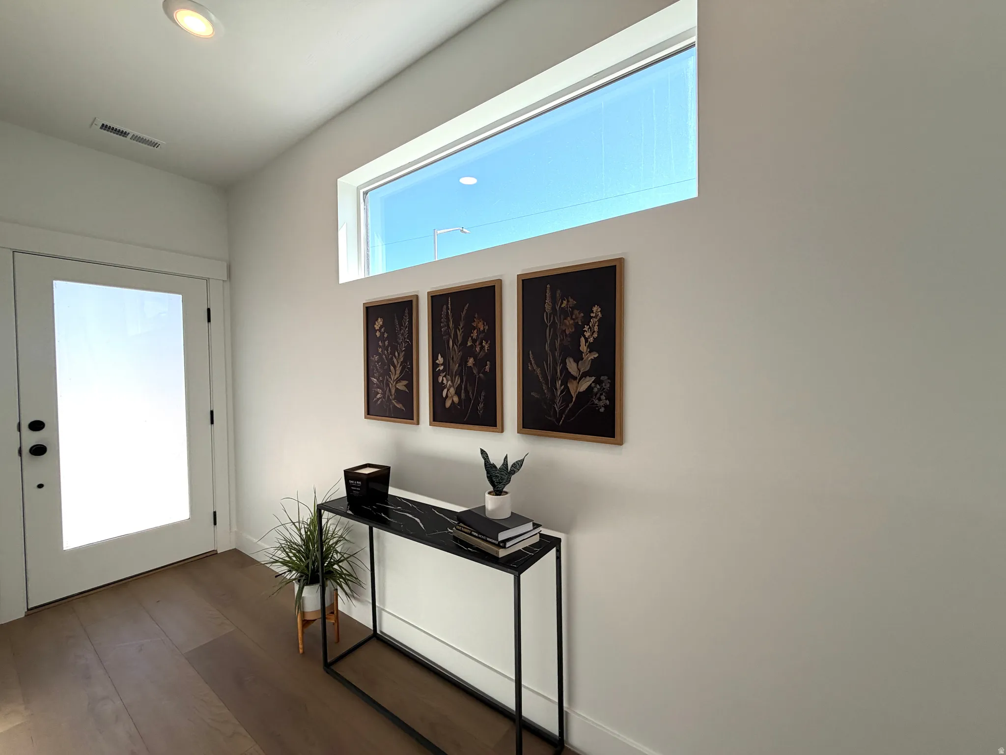 Entryway featuring wood-finish flooring, a full-lite door with matte black hardware, and a high horizontal transom window
