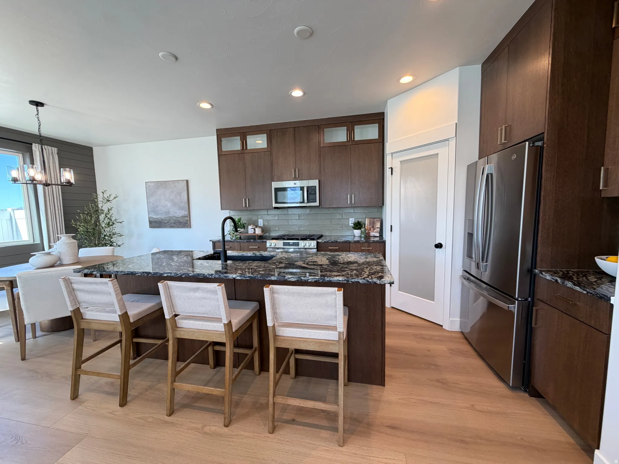 Spacious kitchen featuring an expansive center island with granite countertops, stainless steel appliances, dark wood-finish cabinetry, light wood-finish flooring, and recessed lighting