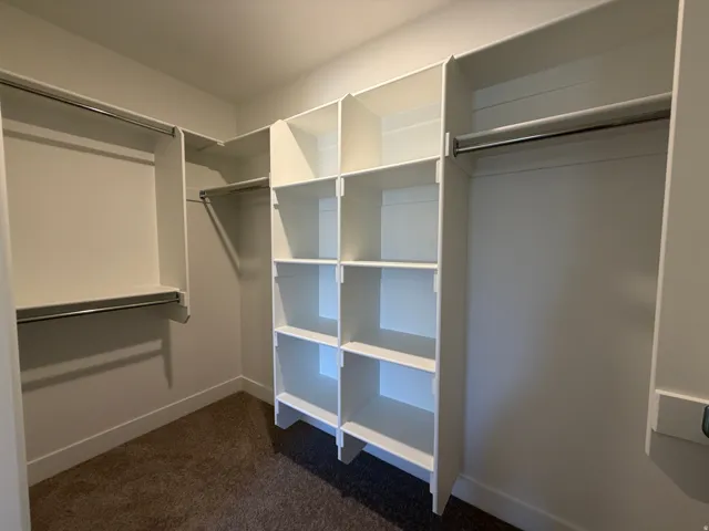 Spacious walk-in closet featuring white built-in shelving, chrome hanging rods, and plush carpet flooring