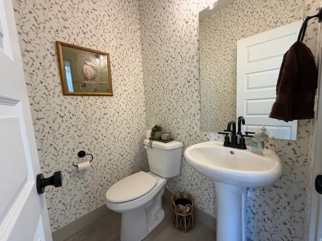 Powder room featuring a pedestal sink with matte black faucet, wall-mounted mirror, and botanical print wallpaper