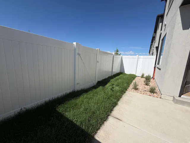 Private outdoor space featuring a full-height white fence, concrete patio, and landscaped area with grass and decorative rocks