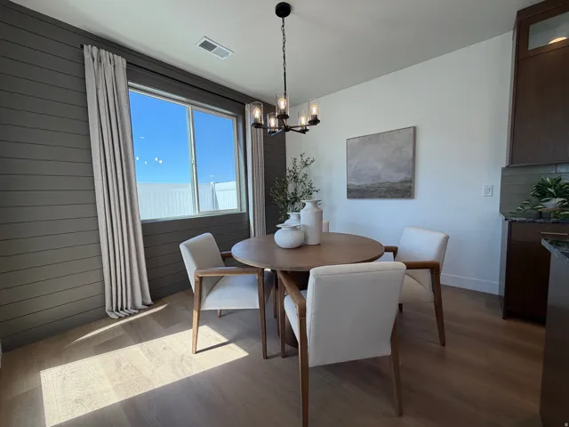 Open-concept dining area featuring light wood-finish flooring, a contemporary chandelier, and a large window with neutral drapery