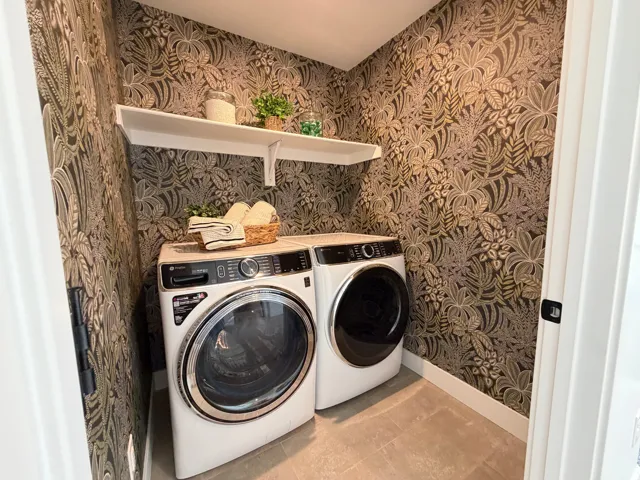 Dedicated laundry area featuring patterned wall covering, tile flooring, and an integrated white shelving unit