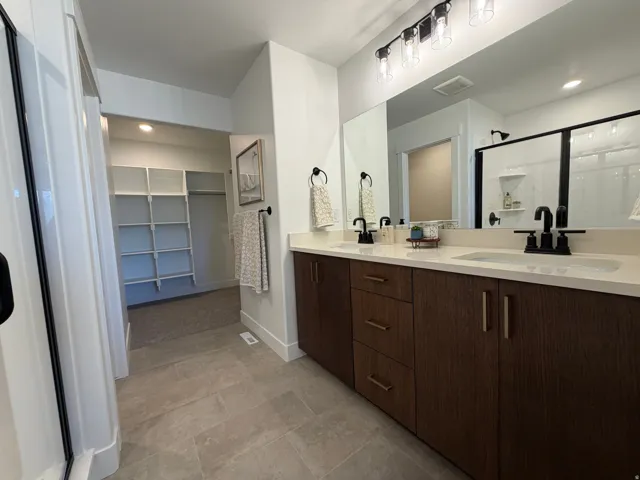 Dual vanity with wood-finish cabinetry, light countertops, and matte black fixtures