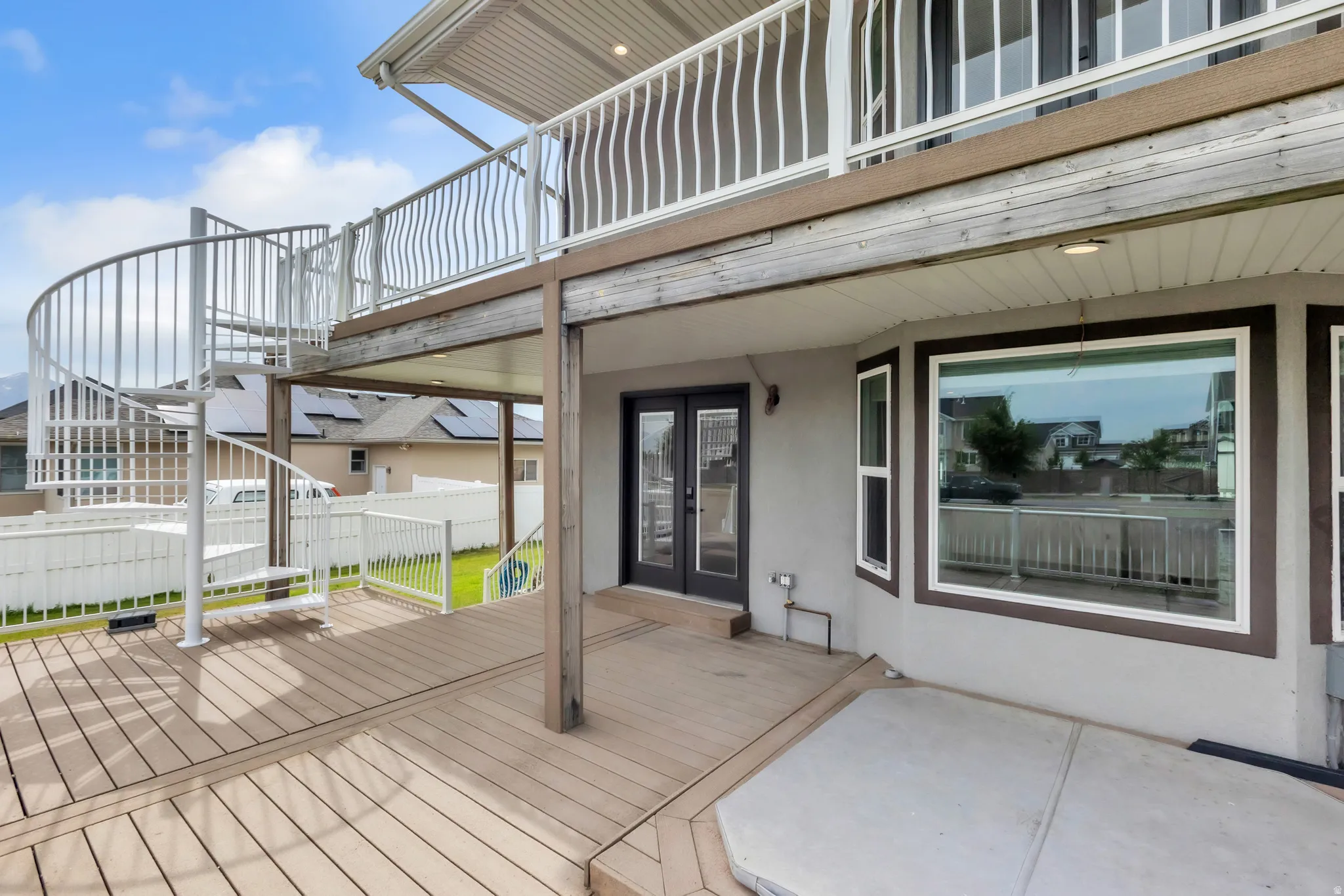 Spacious outdoor deck featuring a spiral staircase, a covered patio area, and a double-door entry