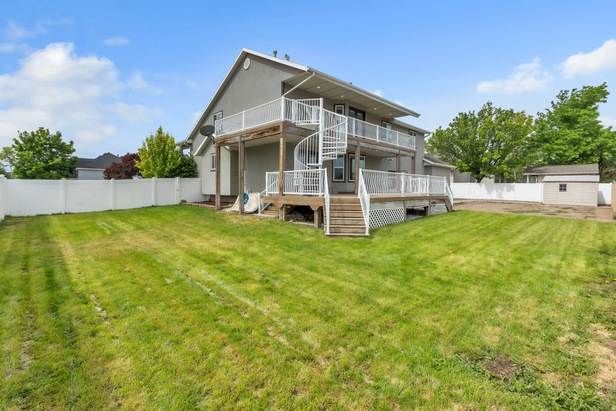Spacious backyard featuring a two-story stucco exterior, upper and lower decks, a spiral staircase, and a white vinyl fence
