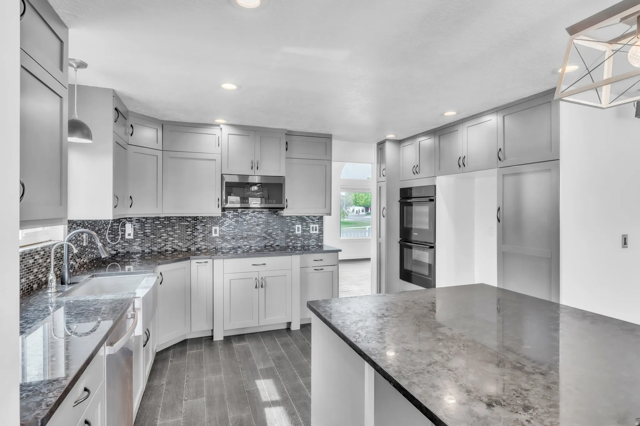 Kitchen featuring grey shaker-style cabinetry, dark granite countertops, a mosaic tile backsplash, wood-finish flooring, and a center island