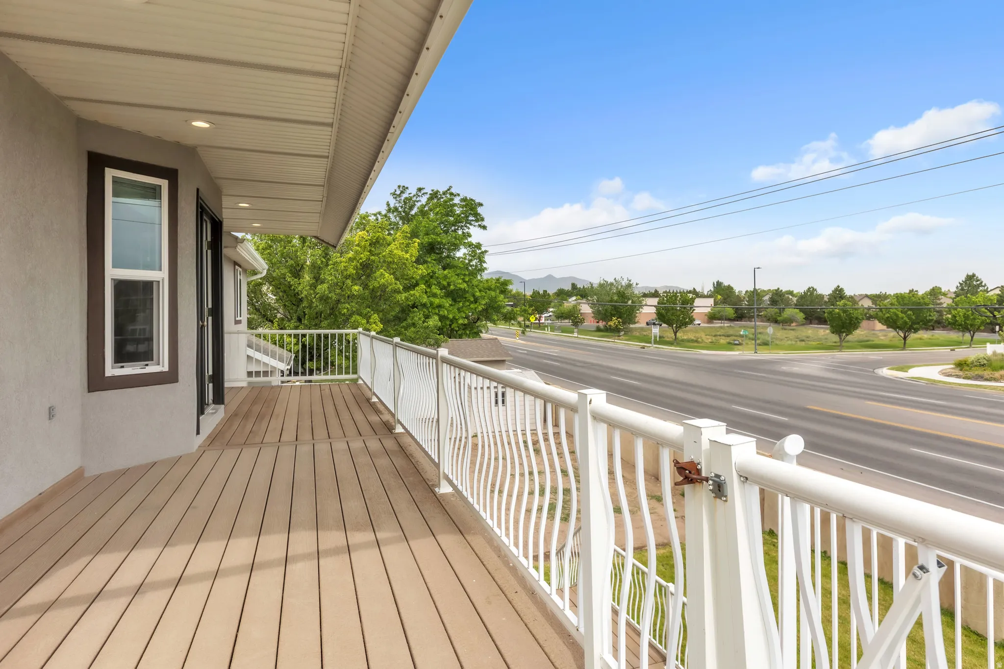 Expansive exterior deck featuring composite decking, white railing with wave-patterned balusters, and recessed soffit lighting