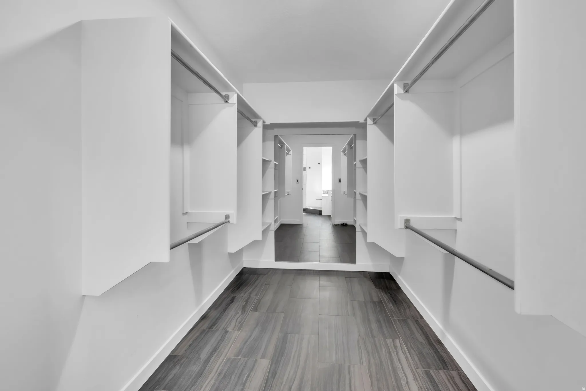 Primary Walk-through closet featuring built-in shelving, hanging rods, wood-finish flooring, and a full-length mirror
