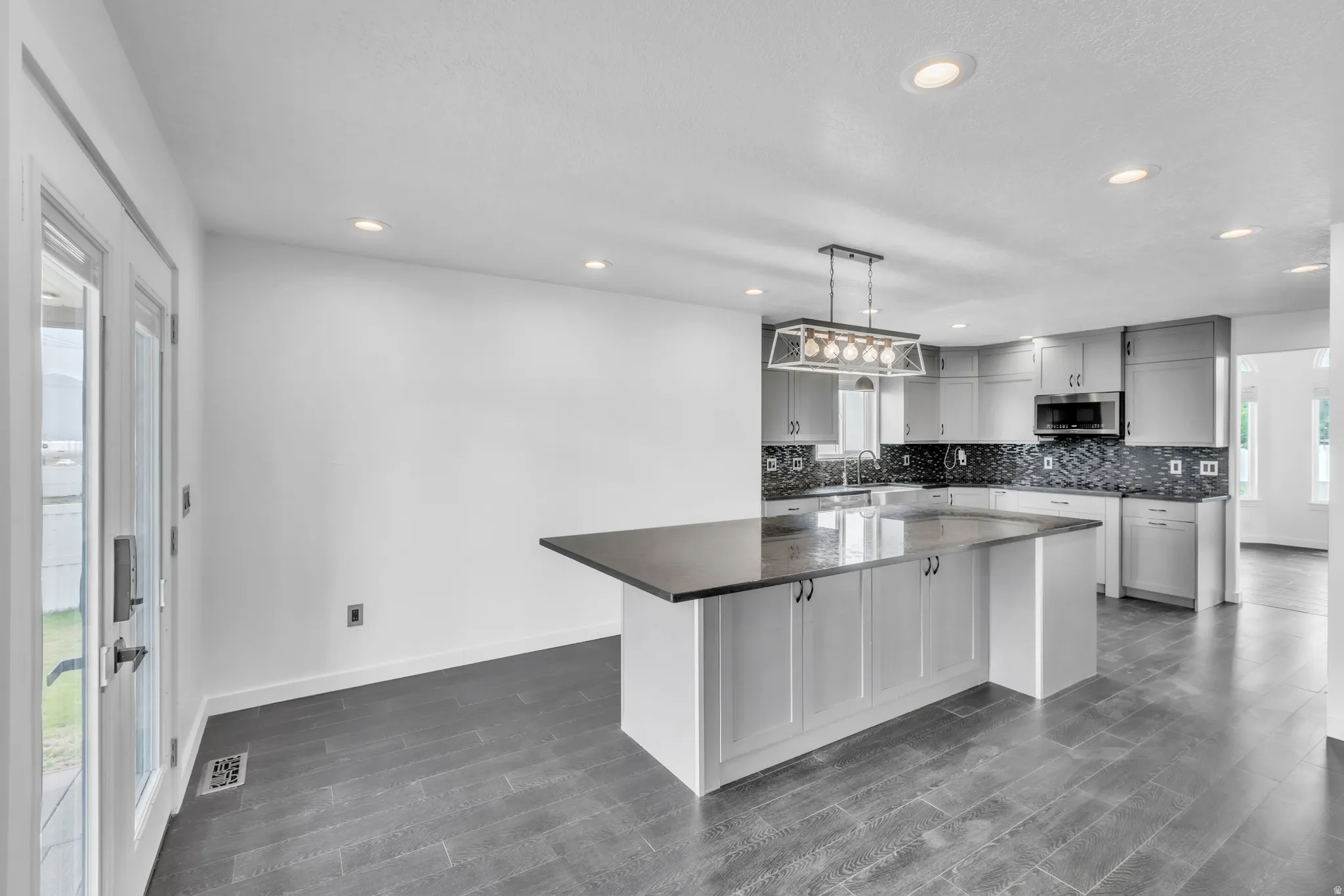 Spacious kitchen featuring an expansive center island with a dark countertop, grey cabinetry, mosaic tile backsplash, and stainless steel appliances