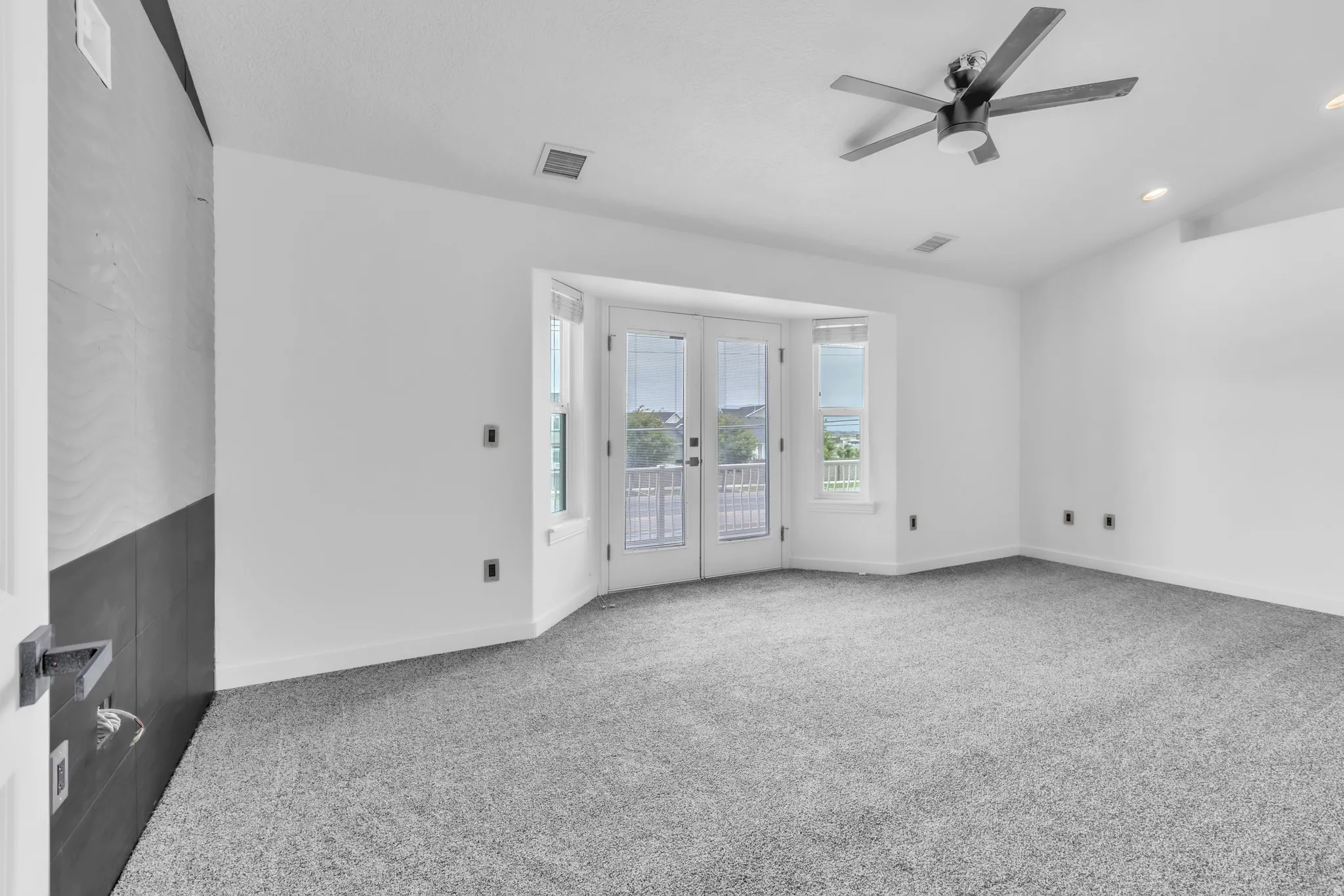 Primary bedroom featuring light gray carpeting, a contemporary ceiling fan, recessed lighting, and a bay window with double doors leading to an exterior balcony