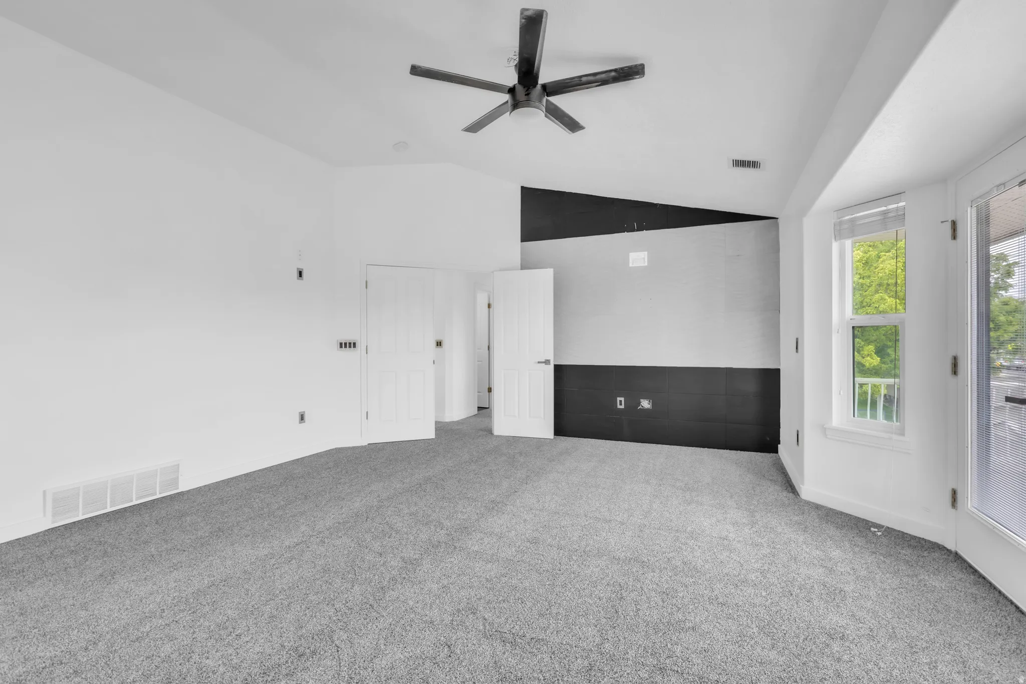 Primary bedroom featuring gray carpet, a contemporary ceiling fan, and a striking accent wall with geometric black and white patterns