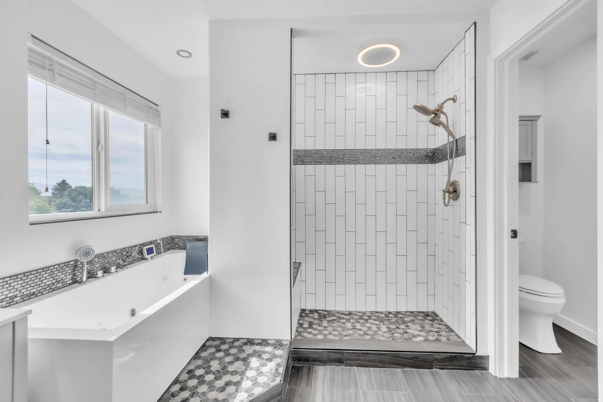 Modern bathroom featuring a soaking tub with tile surround, a walk-in shower with vertical subway tile and pebble floor, and wood-finish flooring