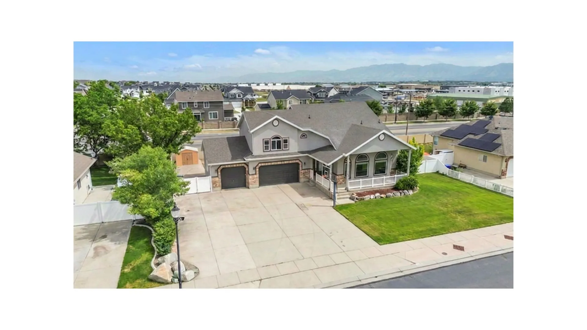Grey stucco exterior with stone accents, featuring a covered porch with white columns, an attached two-car garage, and a concrete driveway