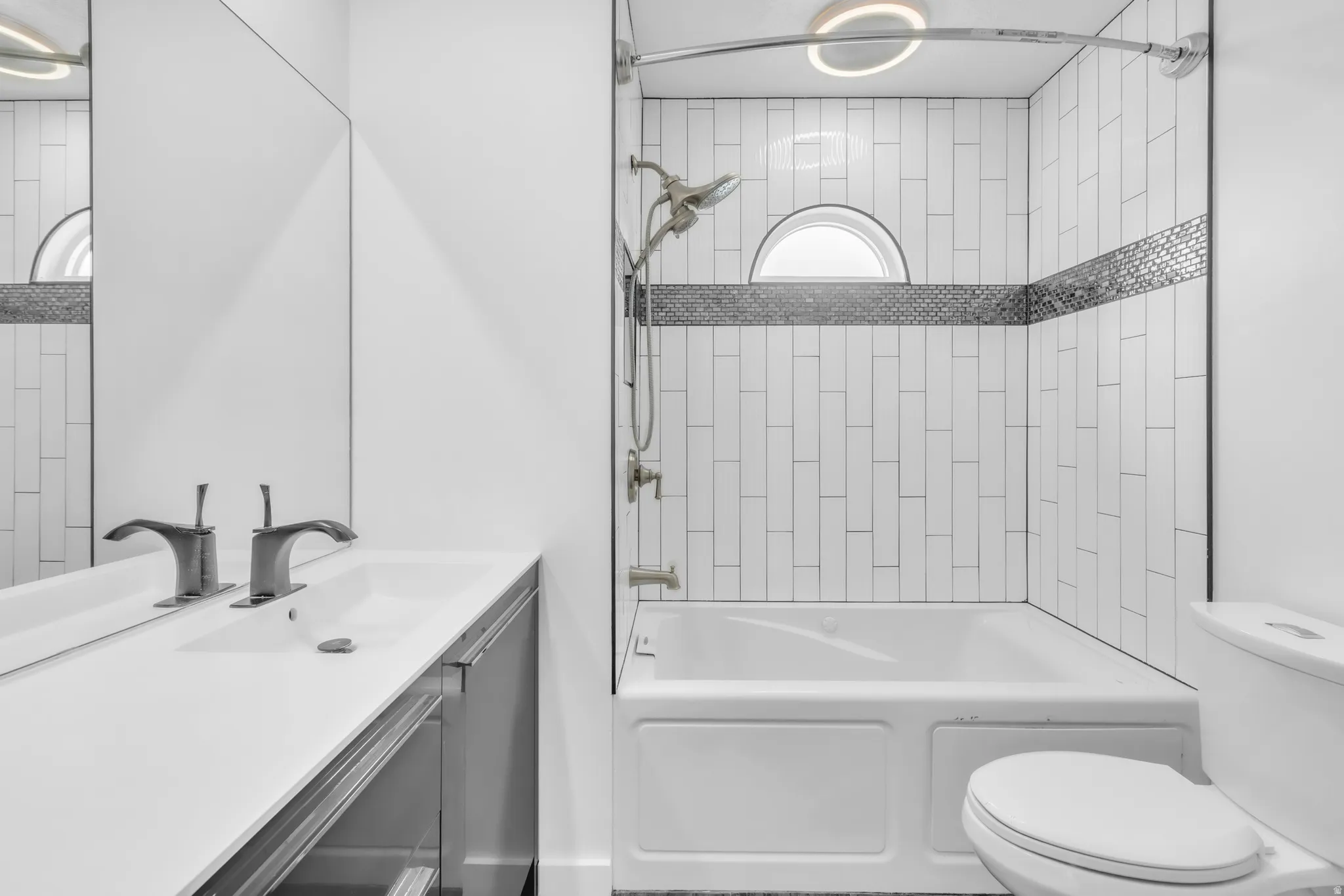 Modern bathroom featuring a full bathtub with subway tile surround, a decorative mosaic tile accent band, and a semi-circular window