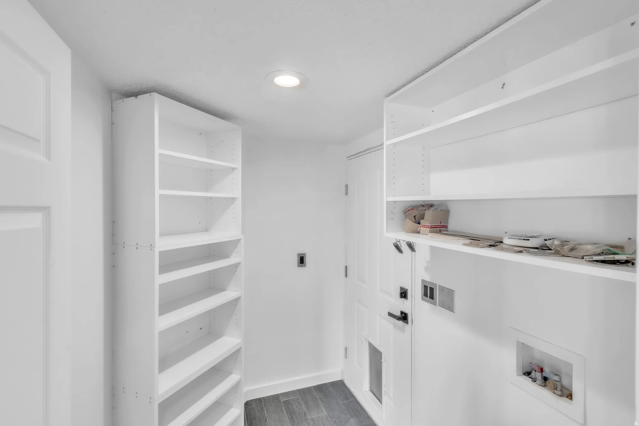 Laundry area featuring white built-in shelving, wood-finish flooring, recessed lighting, and a white paneled door