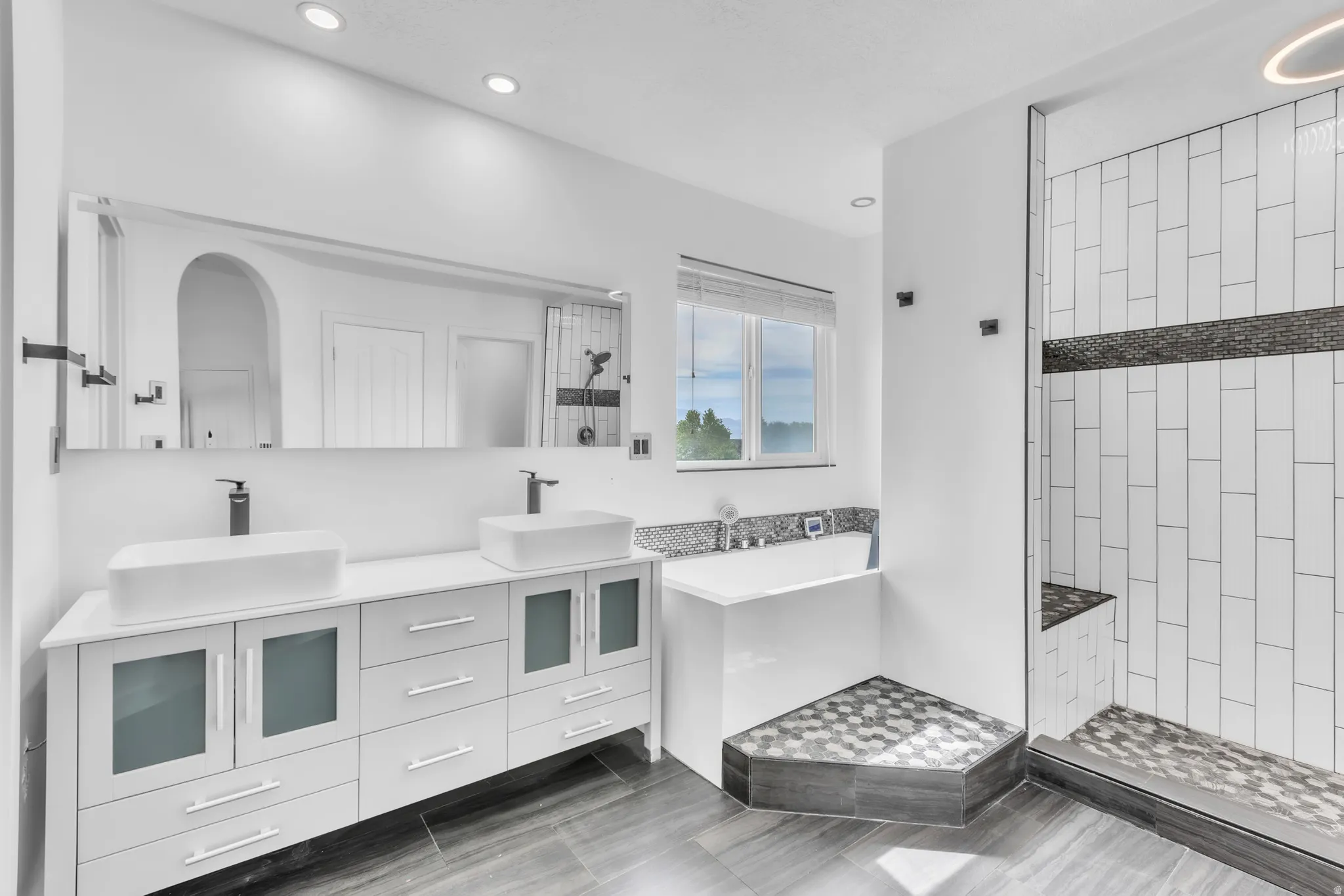 Spacious bathroom featuring a dual vanity with rectangular vessel sinks, a walk-in shower with a built-in bench, a soaking tub, recessed lighting, and large format floor tiling