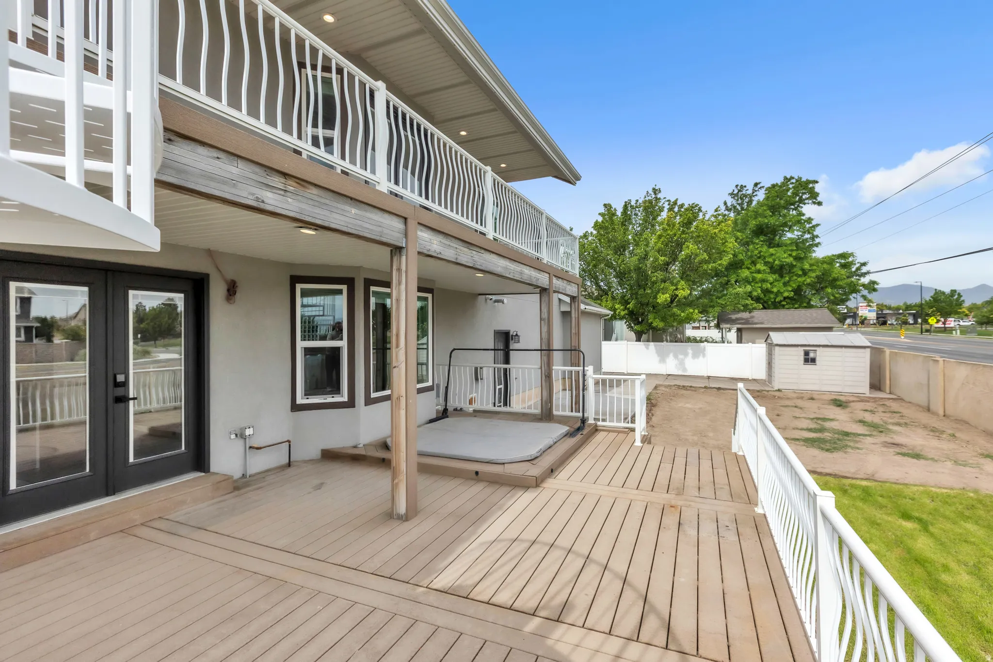 Lower-level deck with composite wood-finish flooring, white railing, and a built-in hot tub