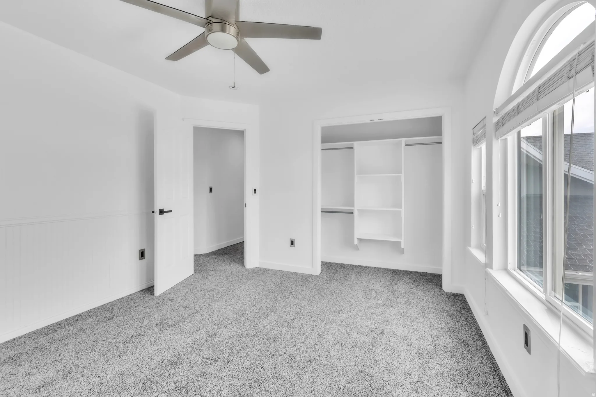 Bedroom featuring a ceiling fan with brushed nickel finish, plush gray carpet, a built-in closet with shelving, and an arched window with blinds
