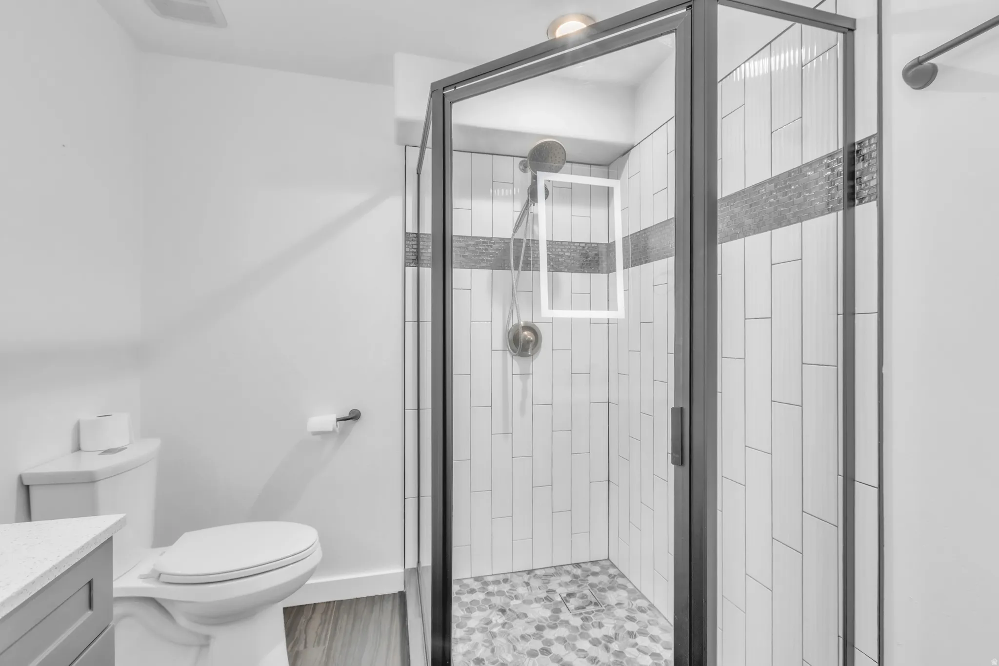 Glass-enclosed shower featuring a black frame, white vertical tile, and a mosaic accent band